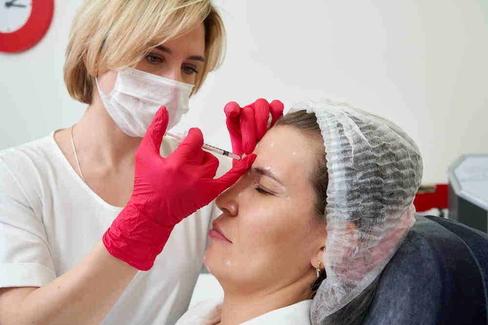 Female cosmetic doctor injects female patient in the forehead. Medazur Medical Clinic.