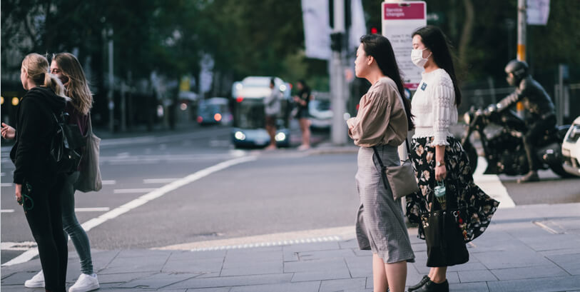 Asian lady wearing surgical mask waits to cross the road with female friend, Medazur Medical Clinic in Leytonstone.